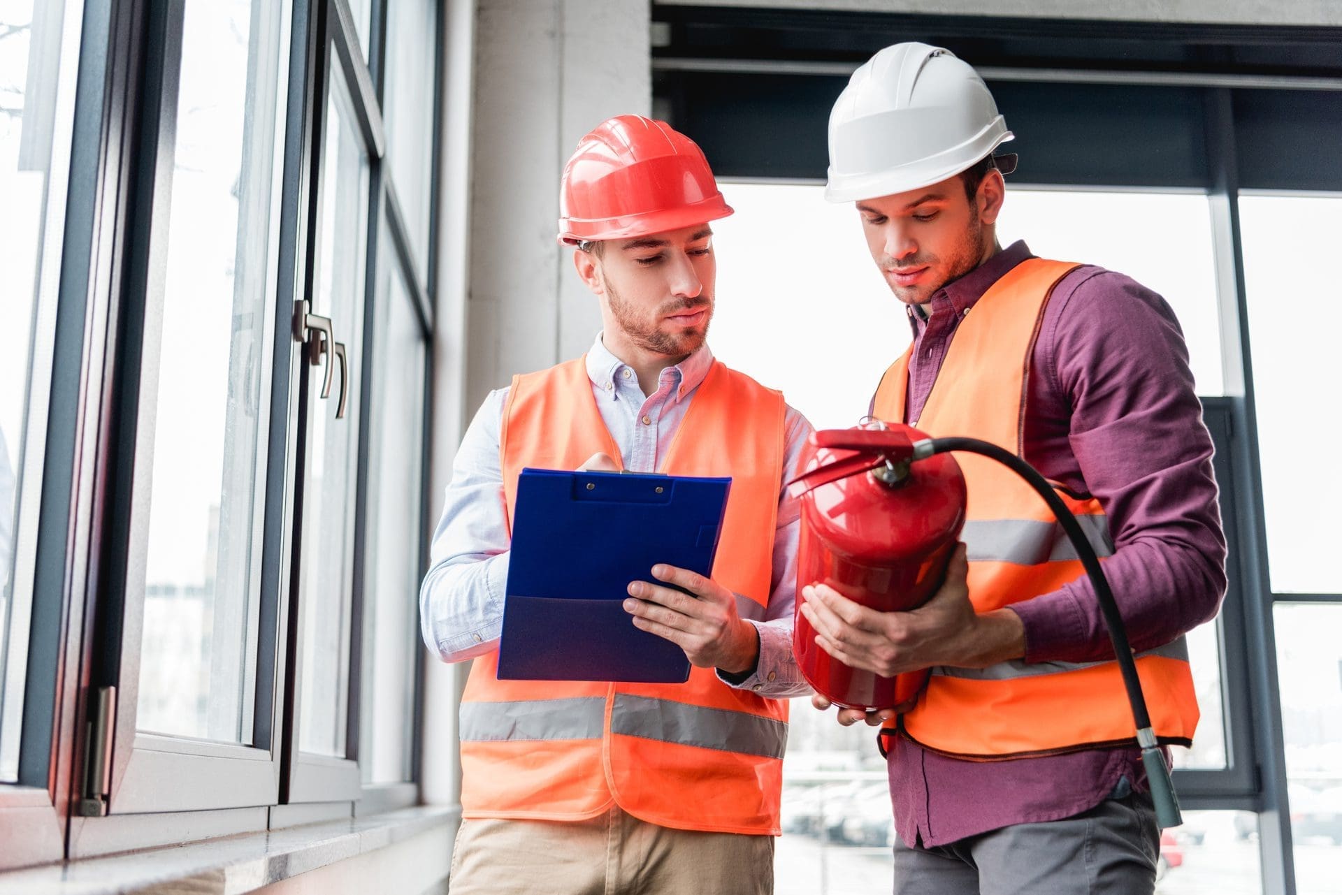 Inspectors in Helmets Standing and Looking at Red Extinguisher